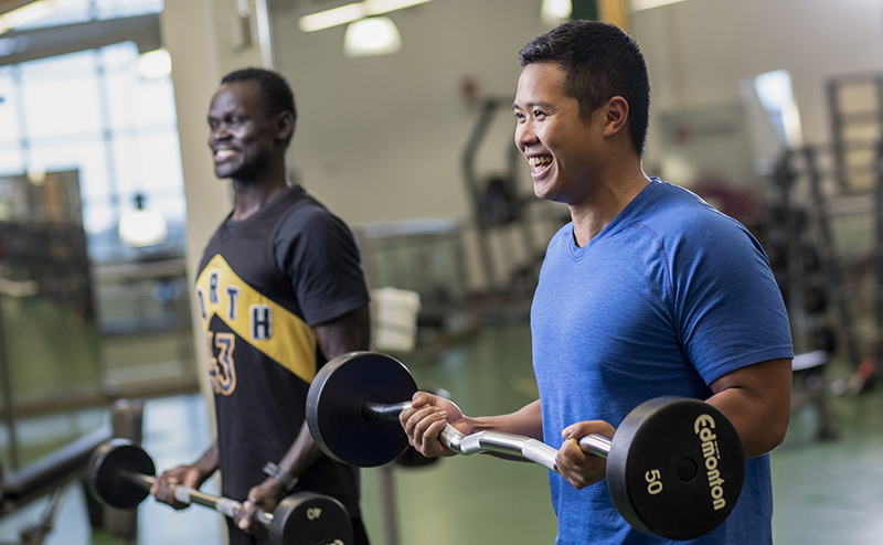 Two men lifting barbells in a fitness centre.